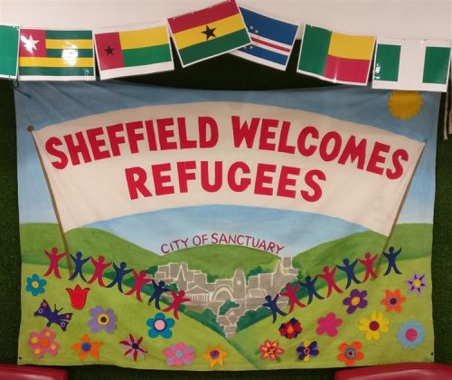 Banner showing Sheffield surrounded by green hills with lots of people carrying a banner saying Sheffield Welcomes Refugees. 