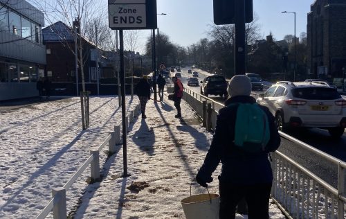 Residents gritting an icy pathway next to a road