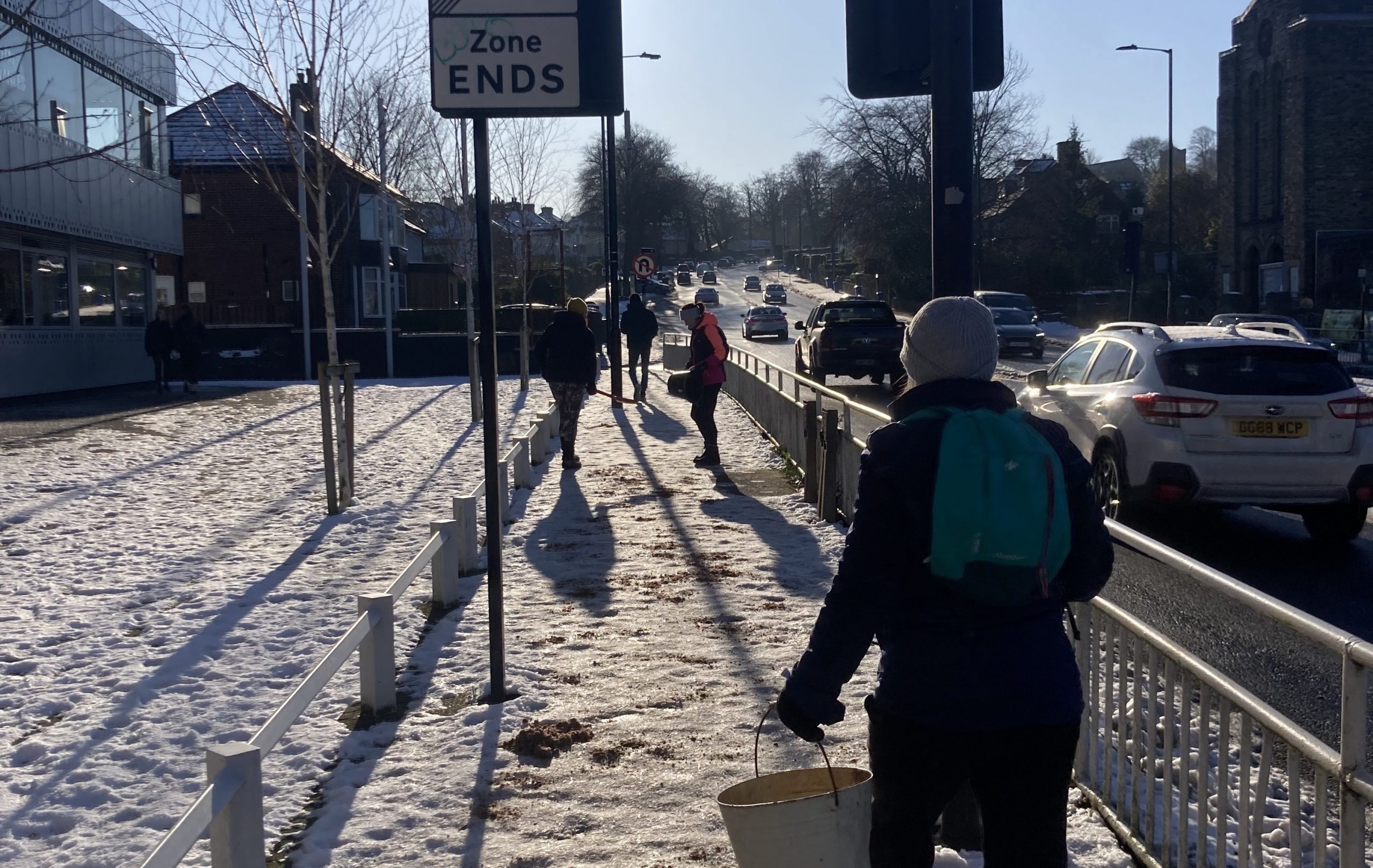 Residents gritting an icy pathway next to a road