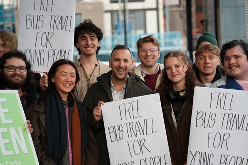Green Party leader Zack Polanski surrounded by young people with placards saying "free bus travel"
